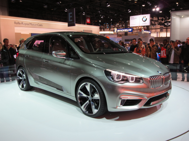 Ein BMW 2er Active Tourer Conceptfahrzeug auf der Frankfurter Motor Show, umgeben von Menschen, die Fotos machen, unter Deckenleuchten mit Texttafeln im Hintergrund.