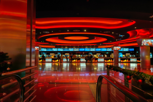 Ein Casino-Innere mit einem Weihnachtsbaum in der Mitte, gefliestem Boden, Geländern auf beiden Seiten, dekorierten Säulen, Deckenleuchten und einer festlichen Menge im Hintergrund.