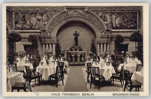 Ein altes Schwarz-Weiß-Foto eines Berliner Restaurants mit Tischen, Stühlen, Blumenvasen, einer Statue, Skulpturen, Pflanzen und Text am unteren Rand.