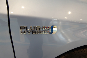 Nahaufnahme eines weißen Autos mit einem "Plug-in Hybrid"-Aufkleber in fetter schwarzer Schrift.