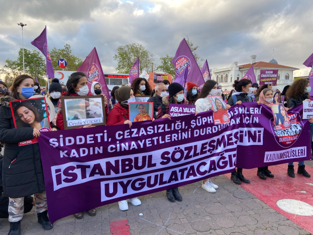 Eine Gruppe von Menschen mit Masken und Schildern und Fahnen protestiert vor einem Gebäude, mit Bäumen, Laternenmasten und einem bewölkten Himmel im Hintergrund, gegen das Verbot von Drogen durch die türkische Regierung.