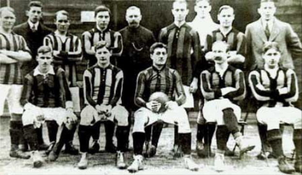 Schwarz-weiß-Foto einer Fußballmannschaft, einige stehen, einige sitzen, vor einer Wand mit dem Text "Ballymena Football Club" unten.