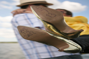 Frauenschuhe mit Datumsangaben darauf, mit einer Person, die eine Frau von hinten hält.
