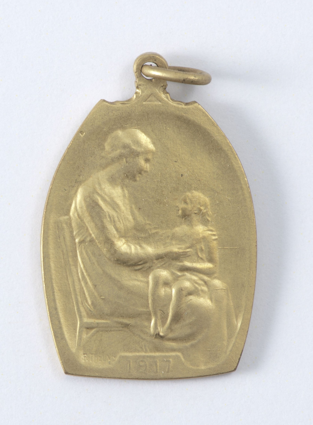 Goldmedaille mit einer Reliefdarstellung einer Frau in einem weißen Kleid mit einem Dutt, die ein Kind hält, beide schauen sich zärtlich an, mit der Inschrift "Mutter und Kind" in Schreibschrift.