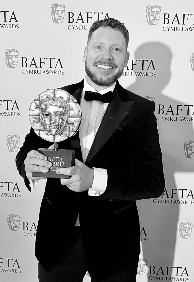 Ein Mann im Smoking hält einen BAFTA-Award und steht vor einer Tafel mit der Aufschrift "BAFTA Awards 2018."