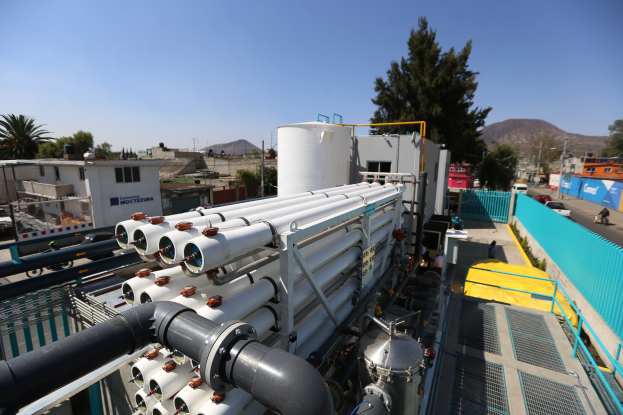 Große Gruppe von Industrieleitungen und Maschinen auf dem Dach eines Gebäudes mit umliegenden städtischen Elementen unter einem klaren blauen Himmel.