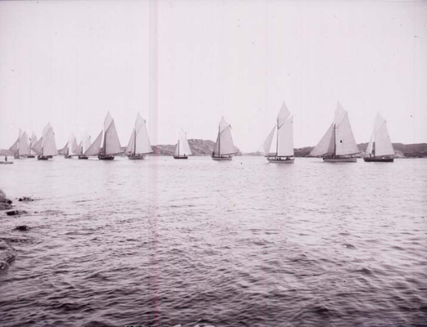 Schwarzes und weißes Foto von Segelbooten auf dem Wasser mit Hügeln im Hintergrund und einem klaren Himmel, beschriftet als New York Yacht Club.