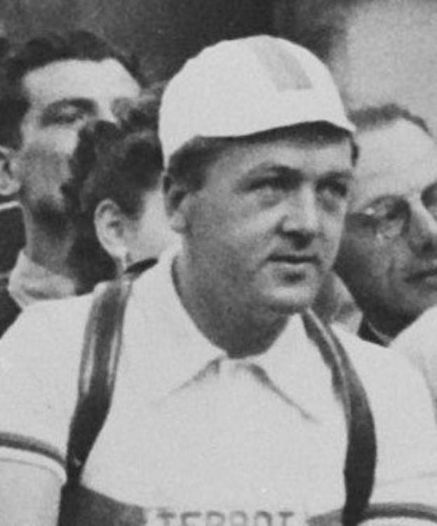 Ein Schwarz-Weiß-Foto eines Mannes in einer Mütze und Hosenträgern, der vor einer Gruppe von Menschen steht, der als legendärer Fußballspieler gilt.