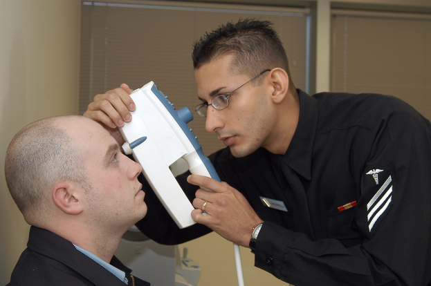 Ein Mann in einem schwarzen Hemd und Krawatte bei einer Augenscreening-Untersuchung durch einen Arzt in einer Brille, der ein Objekt hält, mit Jalousien im Hintergrund.