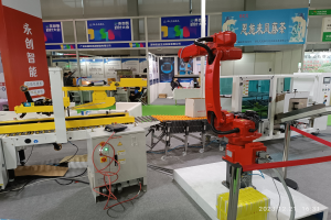 Eine Gruppe von Robotern auf einem Tisch in einer Fabrikumgebung umgeben von Maschinen, Kabeln, Leiterplatten, Beleuchtung und Menschen im Hintergrund.