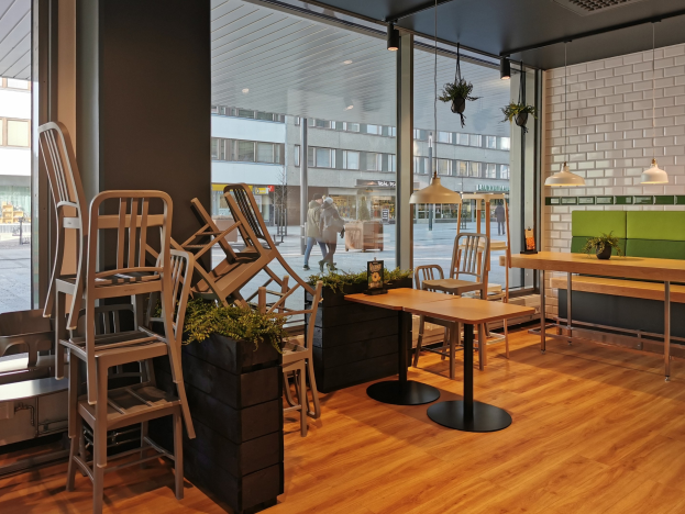 Ein Berliner Restaurant mit Holztischen und -stühlen vor einem großen Fenster, das städtische Außenansichten einschließlich Fußgängern, Gebäuden und Straßenelementen zeigt.