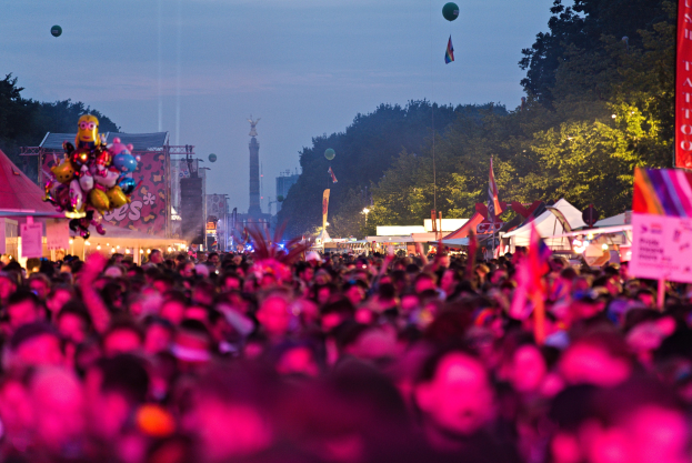 Eine große Menge Menschen auf einem nächtlichen Musikfestival mit bunten Lichtern, Ballons, Zelten, Bannern, Fahnen, Bäumen und einem sternenklaren Himmel im Hintergrund.