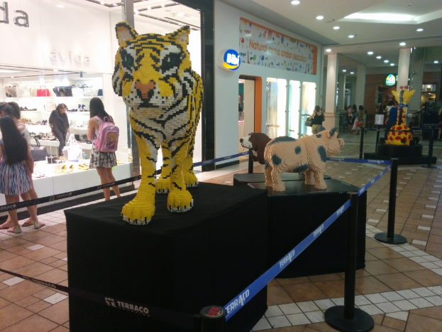 Statuen von Tieren auf schwarzen Boxen umgeben von Pfosten mit elastischen Gurten, mit Geschäften, die Taschen, Schuhe und andere Artikel anbieten, und Menschen, die herumlaufen.
