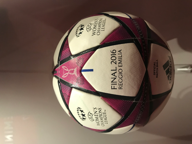Ein weißer Fußball mit schwarzen und pinken Akzenten liegt auf einem hellen Holztisch und zeigt den Text "UEFA Women's Champions League Final 2016."