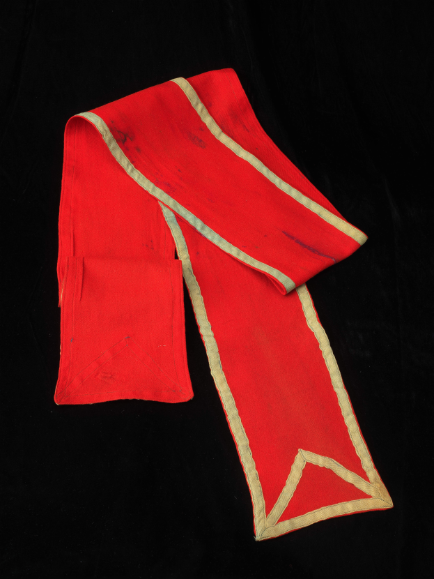 Ein roter Umhang mit goldener Borte auf einem schwarzen Hintergrund.