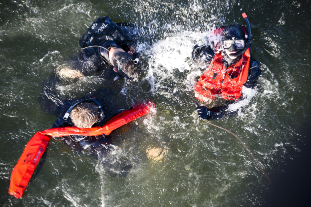 Zwei Personen in Schwimmwesten und Schwimmbrillen im Wasser, eine hält ein Seil, bei einem Wasserrettungs-Training.