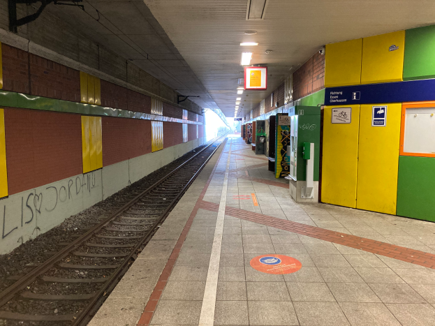 Ein Bahnhof in Berlin, Deutschland, mit einem Zug auf den Schienen, beleuchtet von Deckenlampen, Graffiti an der linken Wand und einigen Gegenständen auf der rechten Seite.