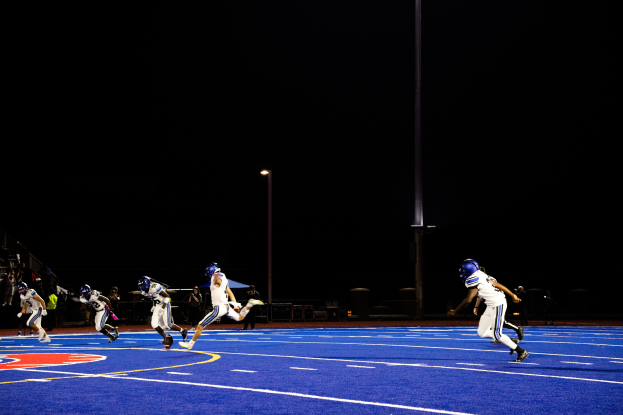 Eine Gruppe von Menschen in Sportkleidung und Helmen, die nachts Fußball spielen, mit Zuschauern im Hintergrund und Text unten auf dem Bild.