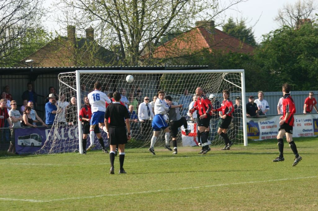 Fußballspieler spielen auf einem Feld mit einem Tor und Zuschauern im Hintergrund.