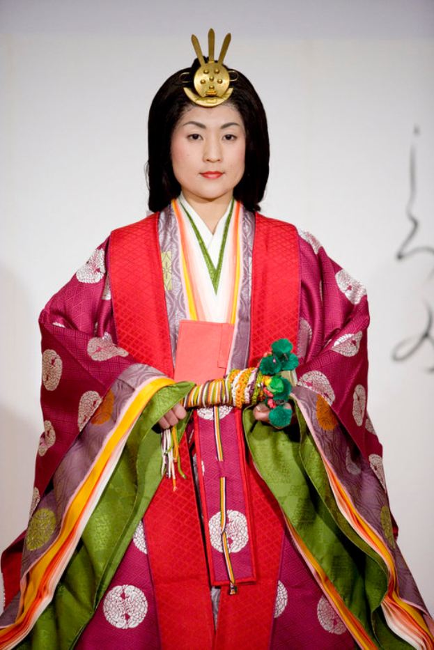 Eine Frau in einem traditionellen japanischen Kimono, mit einem leuchtend roten und grünen Kleid mit aufwändigen Mustern, steht selbstbewusst auf einem Laufsteg mit ihrem Haar zu einem ordentlichen Knoten gebunden.