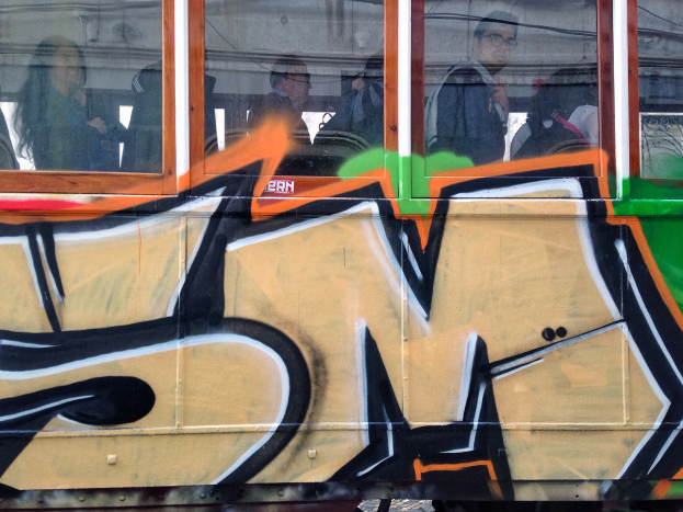Ein Zug mit Graffiti an der Seite, der Passagiere zeigt, mit einem Gebäude und dem Himmel im Fenster gespiegelt.