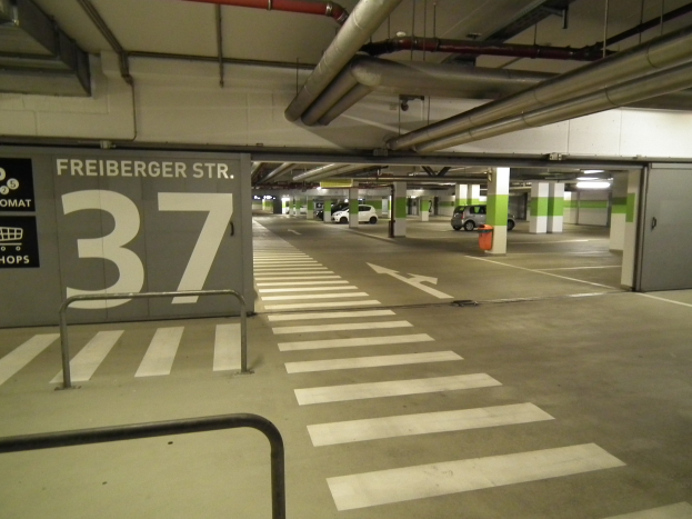 Parkhaus mit einem "Freiburger St." Schild, mehreren geparkten Fahrzeugen, mehreren Säulen, einem Hydranten und einer sichtbaren Decke mit Rohren.