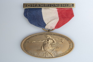 Goldmedaille mit rot-weiß-blauem Band, beschriftet mit 'Meisterschaft' und einem Personenbild.