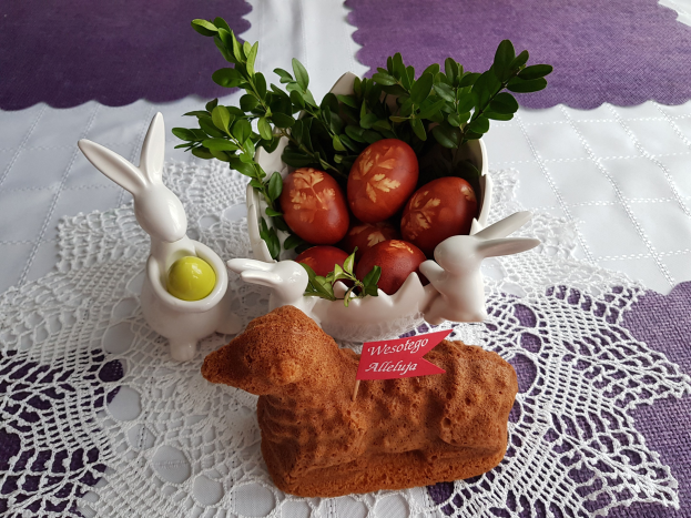 Ein mit einer Decke bedeckter Tisch trägt eine Schüssel voller bunter Ostereier mit Osterhasenfiguren darauf.