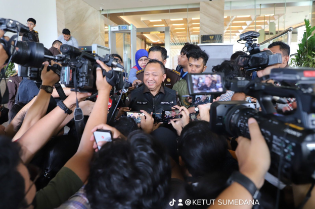 Eine Gruppe von Menschen steht bei einer Pressekonferenz mit Reportern, die Kameras und Handys halten, vor einer Wand, Glastüren, Pflanzen und Deckenleuchten im Hintergrund.