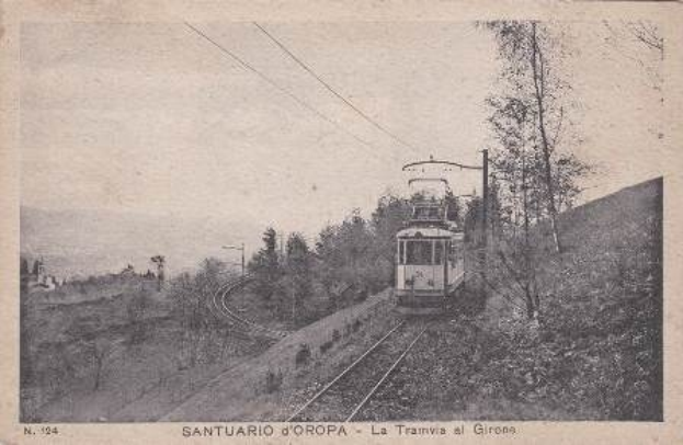 Schwarz-weiß-Fotografie eines Zuges auf Schienen umgeben von Bäumen, Strommasten und Drähten mit Text unten.