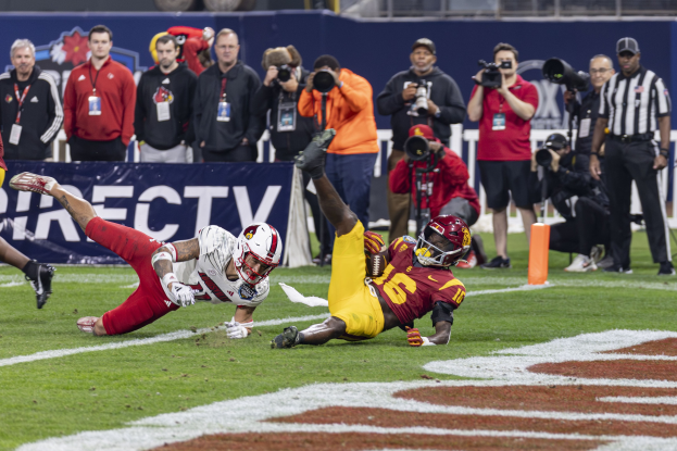 Fußballspieler taucht in die Endzone ein, um einen Touchdown zu erzielen, mit Zuschauern, Fotografen und einem Banner im Hintergrund.