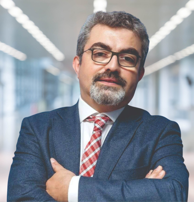 Ein Mann im Anzug und Krawatte mit verschränkten Armen und Brille, der vor einem unscharfen Hintergrund steht, identifiziert als der neu ernannte Marketingchef.