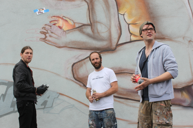 Menschen stehen mit Farbsprühflaschen vor einer Wand mit Graffiti.