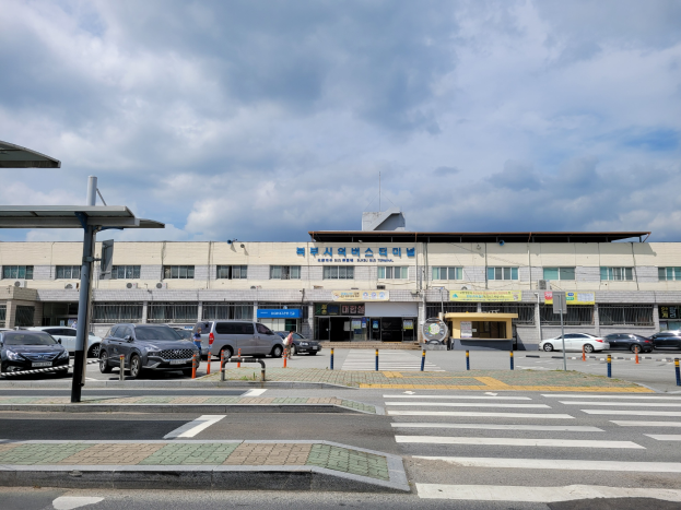 Seoul International Airport, ein großes Gebäude mit parkenden Autos davor, umgeben von Pfählen, Schildern und einem Schuppen, unter einem bewölkten Himmel.