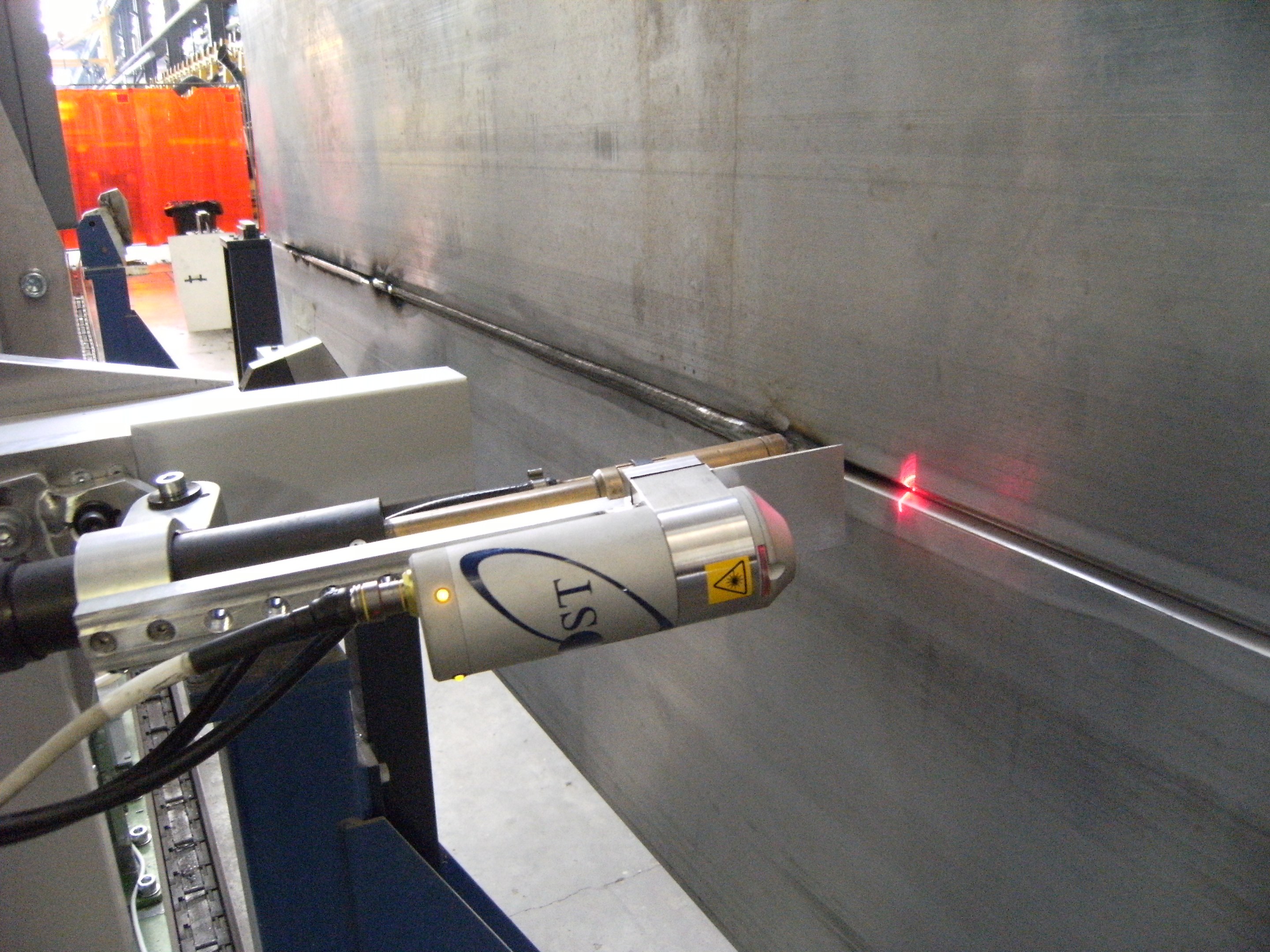 Eine Laser-Schneidmaschine in einer Fabrik, die helles Licht abstrahlt, mit einer Wand auf der rechten Seite und Gegenständen im Hintergrund.