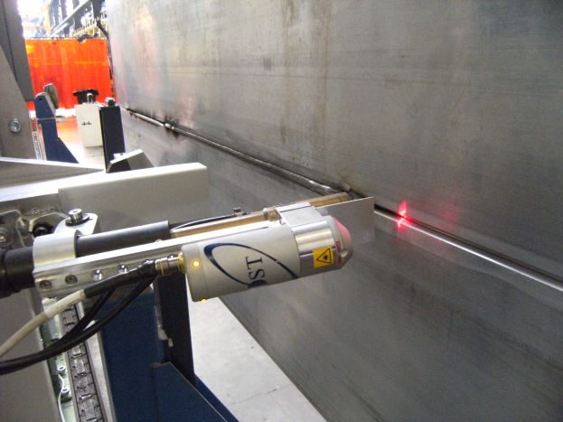 Eine Laser-Schneidmaschine in einer Fabrik, die helles Licht abstrahlt, mit einer Wand auf der rechten Seite und Gegenständen im Hintergrund.