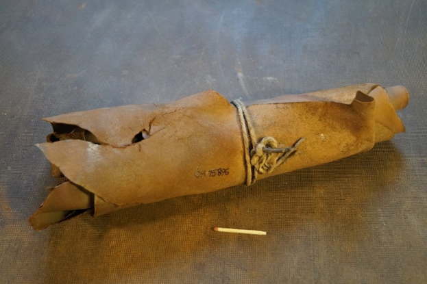 Ein brauner Papiertüte in Form einer Granate, mit einem Seil zusammengebunden, liegt auf einem Tisch mit einer Zigarette daneben.