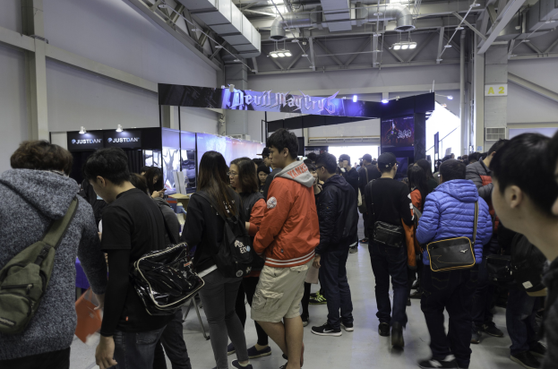 Menschen vor einer Menschenmenge an einer Gaming-Messe mit Texttafeln, Lichtern und Deckenrohren.