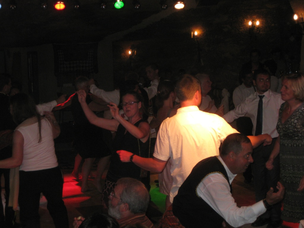 Lebendige Partyszene mit tanzenden Menschen auf dem Boden unter verschiedenen bunten Lichtern in einem dunklen Raum.