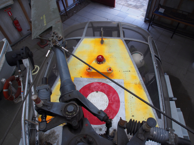 Nahaufnahme eines Hubschraubers auf einem Hallenboden bei Wartungsarbeiten, mit Feuerlöscher links und Bank rechts.