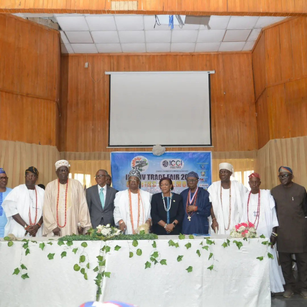 Gruppe von Menschen um einen weißgedeckten Tisch versammelt auf der ICCI International Trade Fair 2019, mit einem Banner, Projektionsschirm und Deckenbeleuchtung im Hintergrund.