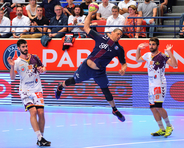 Männer spielen Handball auf einem Court mit einem Ball in der Mitte, Zuschauern im Hintergrund und verstreuten Kleidungsstücken um den Court herum, mit einem Banner mit der Aufschrift "Futsal-Weltmeisterschaft 2015 - Paris Saint-Germain vs. Olympique Lyon".