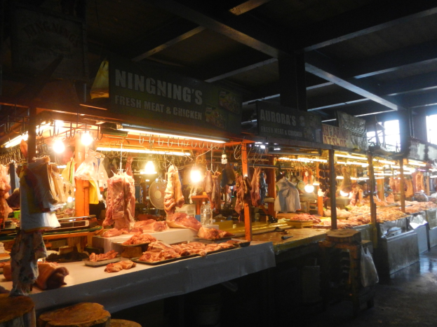 Ein Schlachthaus-Vitrine voller verschiedener Fleischsorten, beleuchtet von Deckenlampen, mit Texttafeln und Hockern im Shop sichtbar.