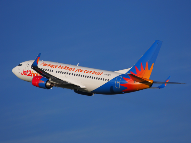 Ein Jet2holidays Airbus A320-200-Flugzeug im Flug, mit einer weiß-blauen-orangen-roten Lackierung gegen einen blauen Himmel.