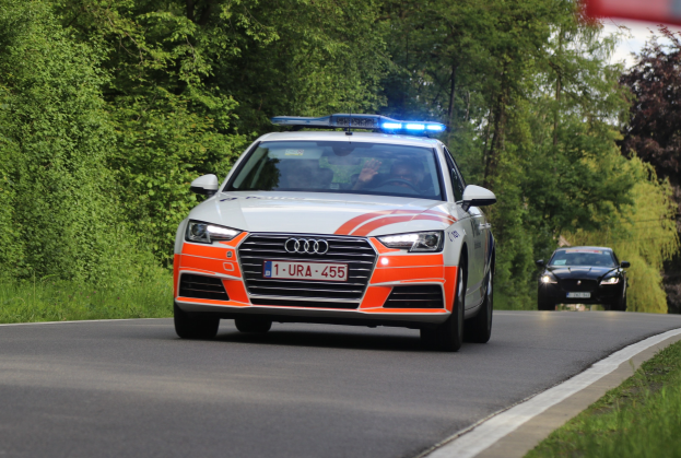 Ein Polizeiaudi A4 mit zwei Insassen fährt auf einem grasbewachsenen Weg neben einem Wald unter einem klaren blauen Himmel.