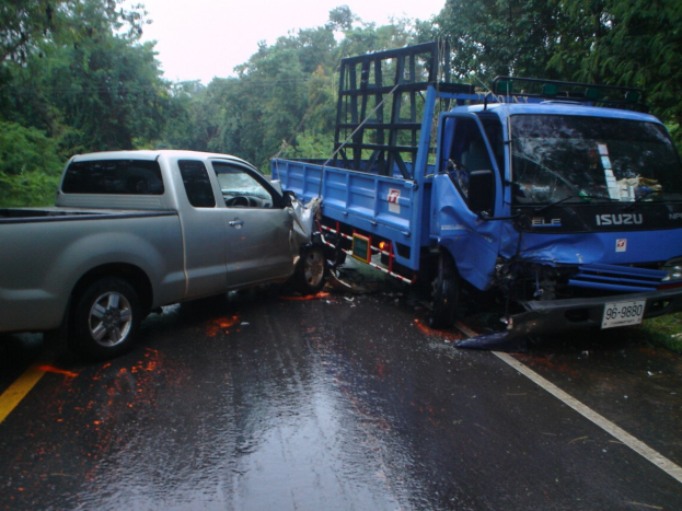 Ein schwerbeschädigter Lkw mit eingedellter Front und verbeulter Karosserie am Straßenrand, umgeben von Bäumen unter einem klaren blauen Himmel.