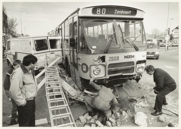 Schwarzes und weißes Foto eines auf der Straße gestrandeten Busses mit Menschen und Werkzeugen in der Nähe, vor Häusern, Bäumen und Masten.