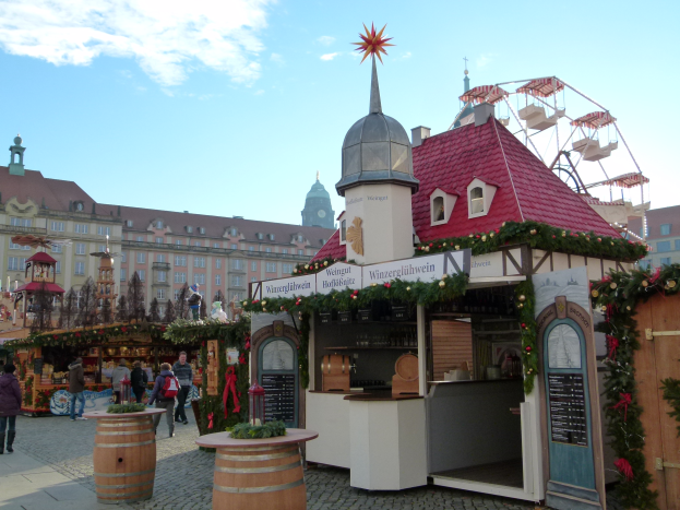 Ein lebendiger Weihnachtsmarkt in Nürnberg, Deutschland, mit Menschen um geschmückte Buden, Gebäude, ein Riesenrad und eine Tafel auf der rechten Seite.