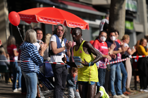 Ein Mann in einem gelben T-Shirt läuft durch eine Menge bei einem Marathon, während die Menschen im Hintergrund klatschen und jubeln.