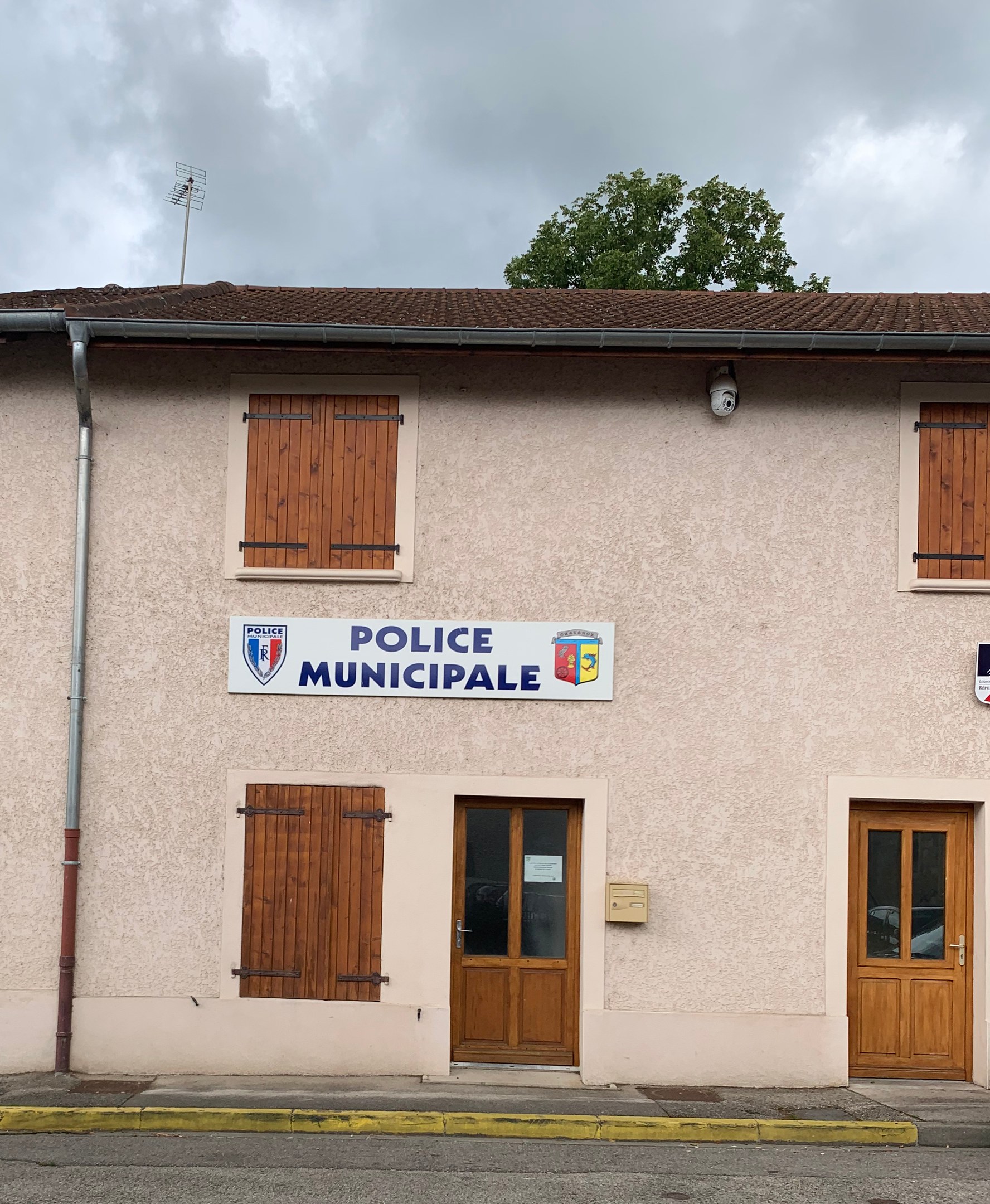 Polizeigebäude mit einem Schild, Fenstern, Türen, einer Namensschilder, einem Rohr, einem Baum und einem bewölkten Himmel im Hintergrund.